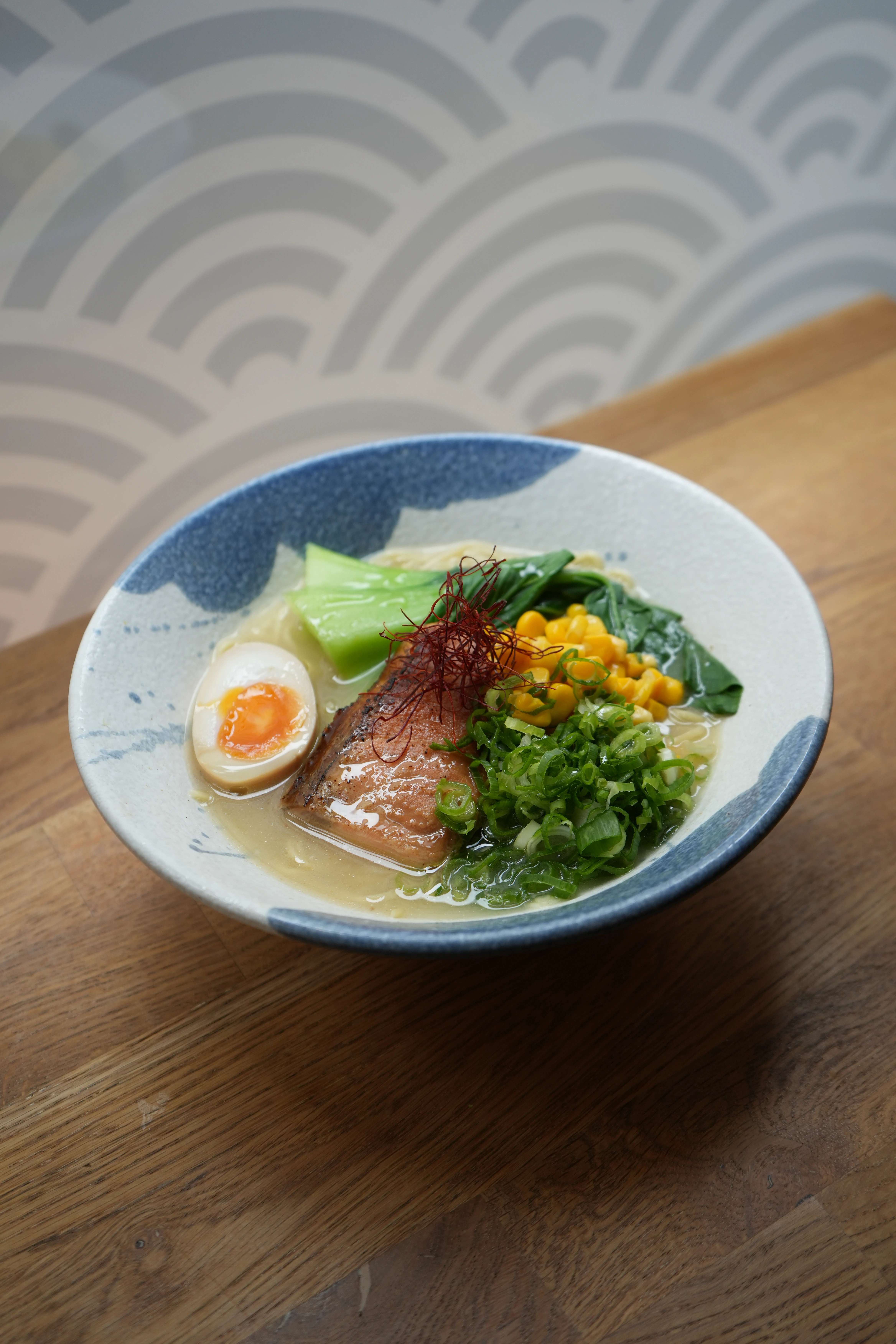 Nahaufnahme von Ramen mit Lachs, Ei, Mais und Gemüse in einer dekorativen Schale.